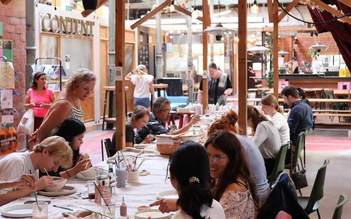 Deelnemers schilderen keramiek aan een lange tafel tijdens een Sip 'n Glaze event in Hal5 Leuven